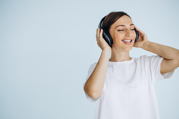 青の背景に分離されたワイヤレス ヘッドフォンで音楽を聴く白いシャツの若い女性