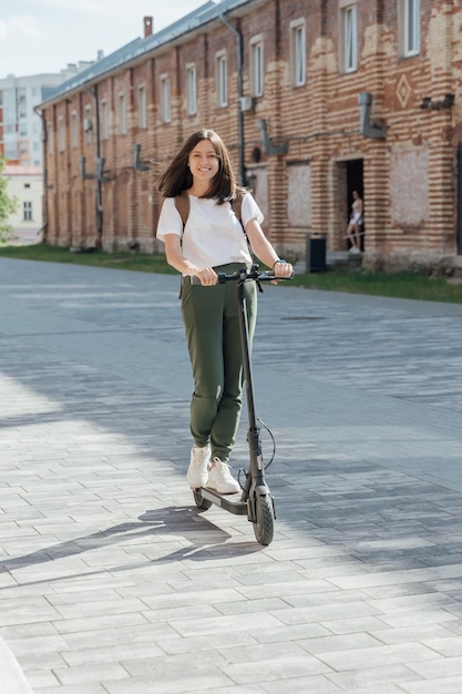 Young woman in white sneakers riding electric scooter on urban street
