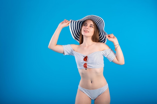 Young woman in white striped swimsuit lingerie and striped hat isolated on blue background