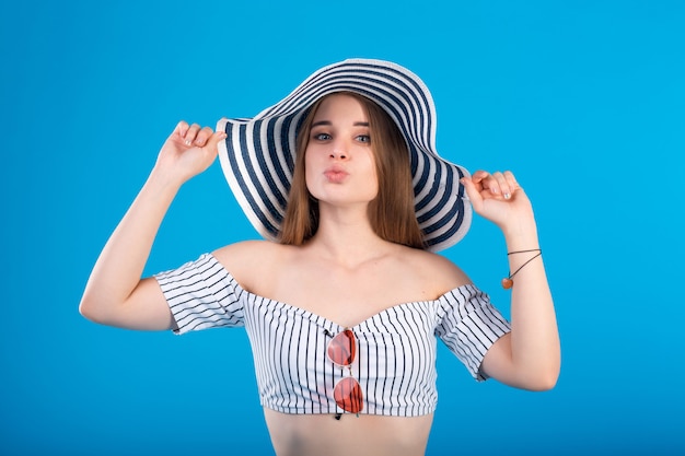 Young woman in white striped swimsuit lingerie and striped hat isolated on blue