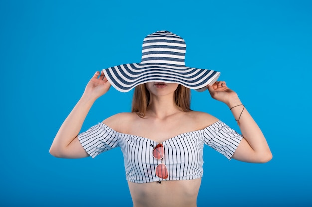 Young woman in white striped swimsuit lingerie and striped hat to lips isolated