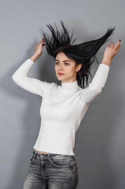 Young woman in a white sweater throws up her black hair