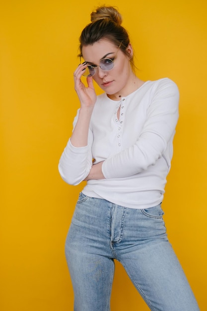 Foto una giovane donna con una felpa bianca e jeans blu si trova in studio su uno sfondo giallo