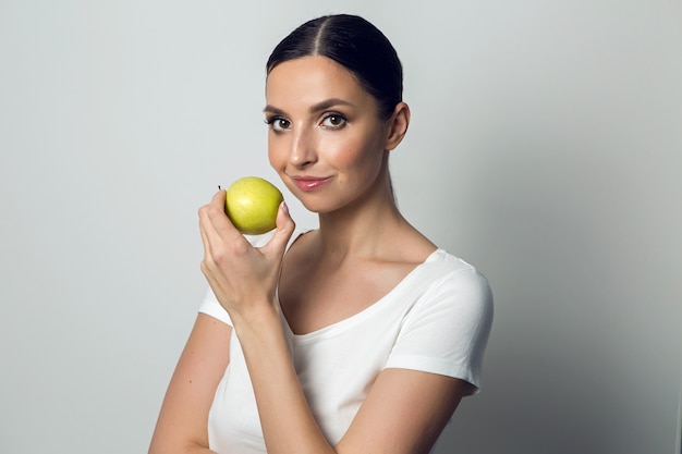 Young woman in a white t-shirt with green apple on white background