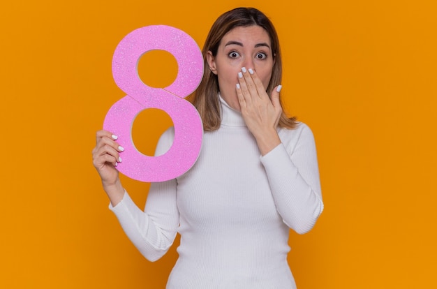 young woman in white turtleneck holding number eight