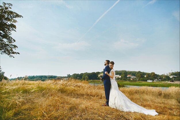 Young woman in a white wedding dress and brutal handsome man in a blue business suit posing outdoors