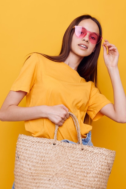 Young woman wicker bag in hand pink glasses yellow background