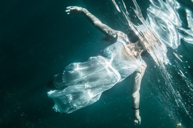 A young woman will dive with a white dress swimming underwater image summer