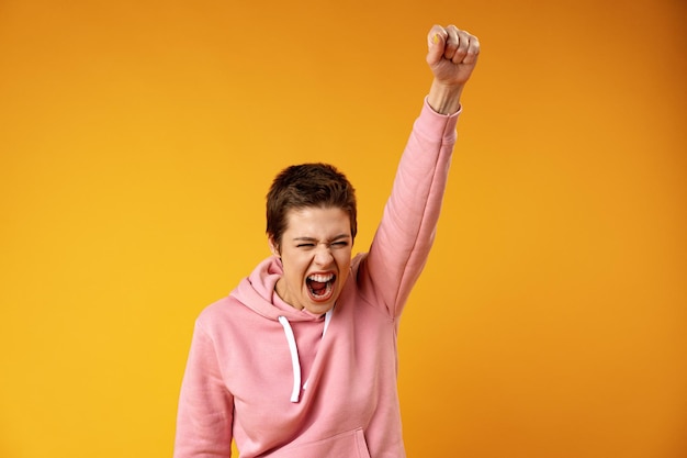 Young woman winner raising fist after a victory over yellow background