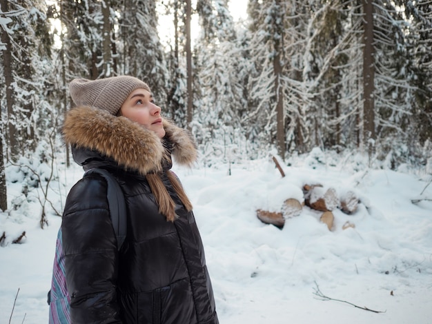 모피 후드가 달린 겨울 다운 재킷을 입은 젊은 여성이 겨울에 숲을 걷습니다. 아름다운 서리가 내린 자연, 눈 속의 소나무 숲.