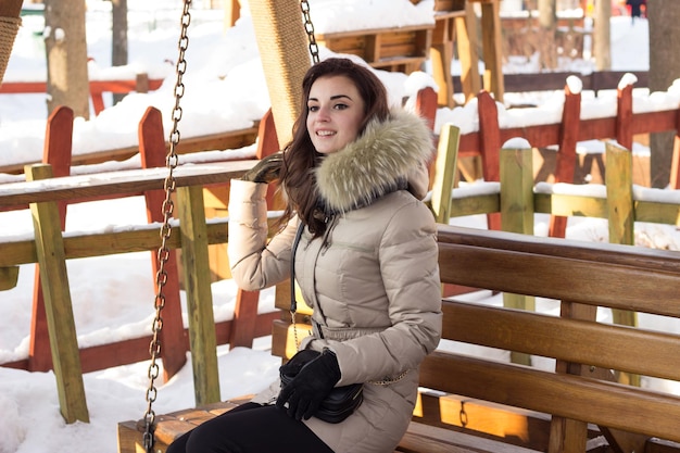 Young woman in winter park sitting on bench with a lot of snow around