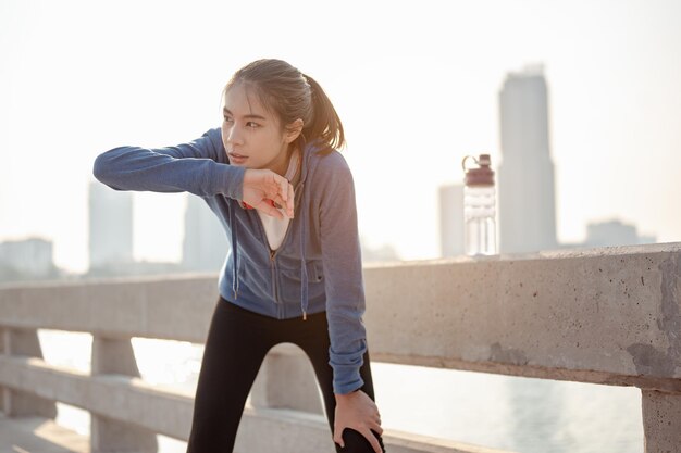 Young woman wipes sweat after a morning workout in the city. A city that lives healthy in the capital Rear view of the city Exercise, fitness, jogging, running, lifestyle, healthy concept.