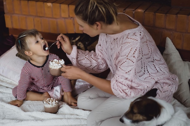 写真 暖炉のそばで子供を持つ若い女。ママと息子は暖炉のそばのマシュマロとココアを飲みます。