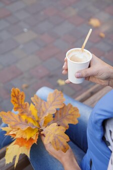 커피 한 잔과 가을 단풍잎을 들고 있는 젊은 여성