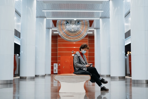 Фото Молодая женщина со смартфоном сидит на скамейке в метро