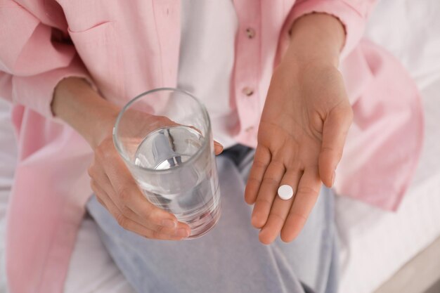 Young woman with abortion pill and glass of water on bed closeup