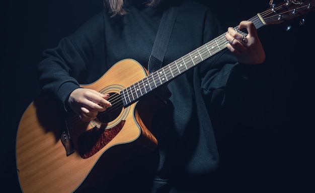 A young woman with an acoustic guitar in the dark under a ray of light