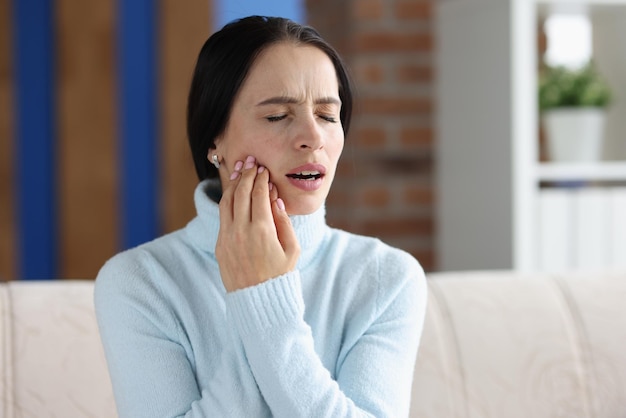 Young woman with acute toothache on couch inflammation of gums and problem with teeth concept