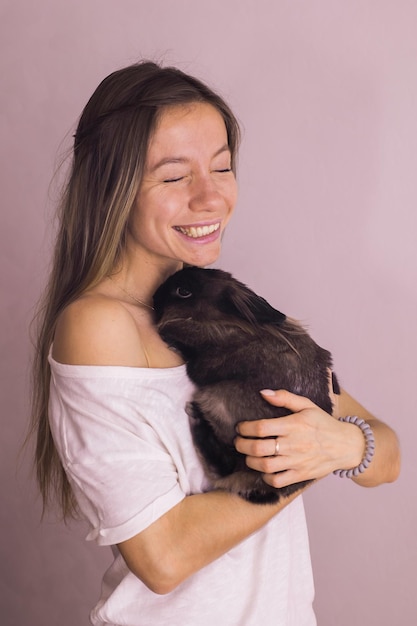 실내에 사랑스러운 토끼를 안고 있는 젊은 여성은 사랑스러운 애완동물과 동물 개념을 닫습니다