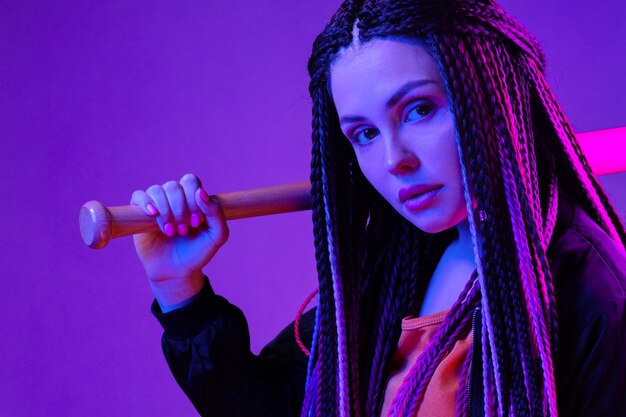 Photo young woman with afro braids holding a bit on a shoulder in neon lught