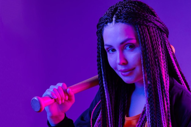 Photo young woman with afro braids holding a bit on a shoulder in neon lught