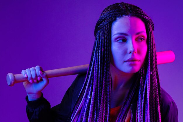 Photo young woman with afro braids holding a bit on a shoulder in neon lught