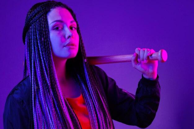 Photo young woman with afro braids holding a bit on a shoulder in neon lught