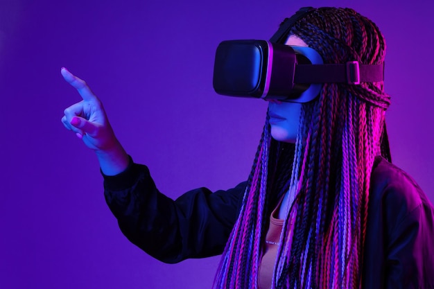 Young woman with afro braids using vr glasses on dark purple neon background