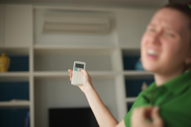 Young woman with air conditioner remote control using air conditioner at home girl is cooling off