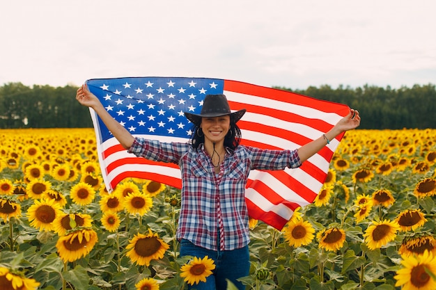 ひまわり畑でアメリカ国旗を持つ若い女性