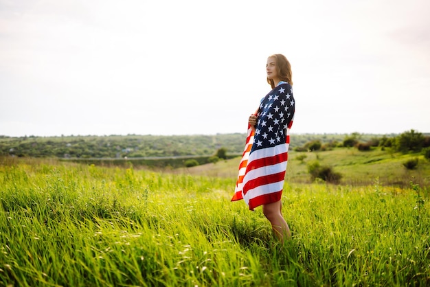 Young woman with american USA flag on blooming meadow Independence Day 4th July