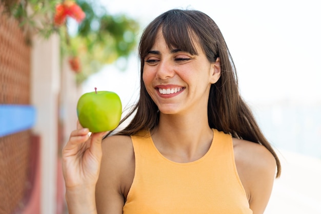 屋外で幸せな表情でリンゴを持つ若い女性