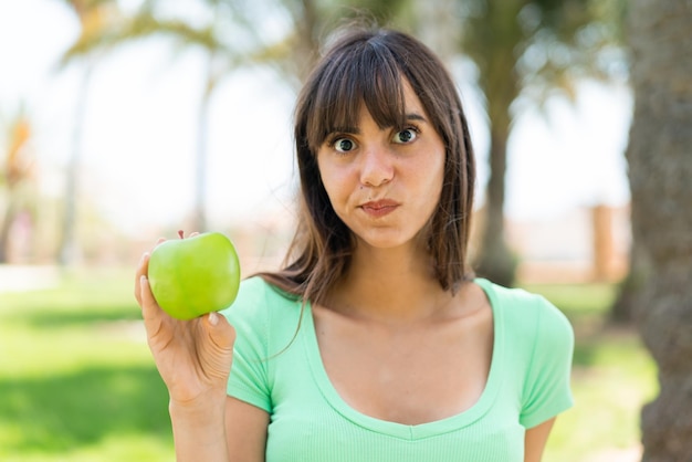 Young woman with an apple at outdoors with sad expression