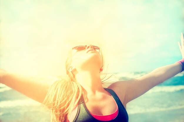 Young woman with arms outstretched at beach against sky