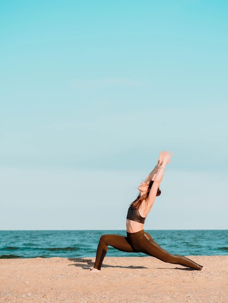 young woman with arms raised on beach against sky