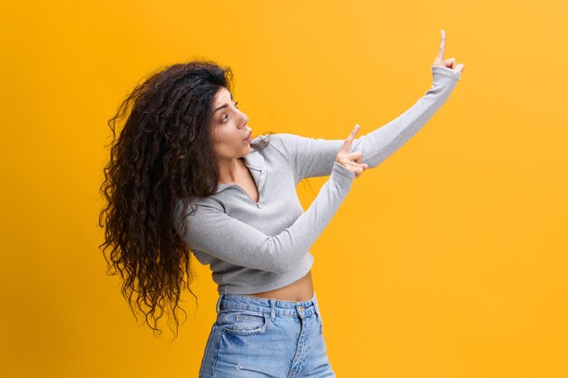 Foto giovane donna con le braccia alzate in piedi contro uno sfondo giallo