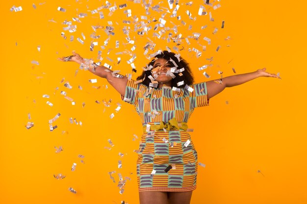 Young woman with arms raised standing against yellow wall