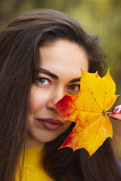 가을 잎을 손에 들고 가을 노란 단풍 정원 배경을 가진 젊은 여성