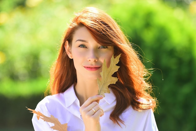 Young woman with autumn leaves in hand and fall yellow maple