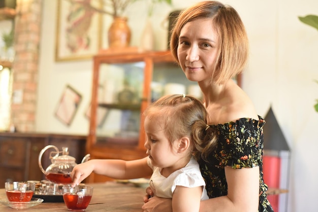 Young woman with a baby girl drinking tea from a tea pot in a coffee shop