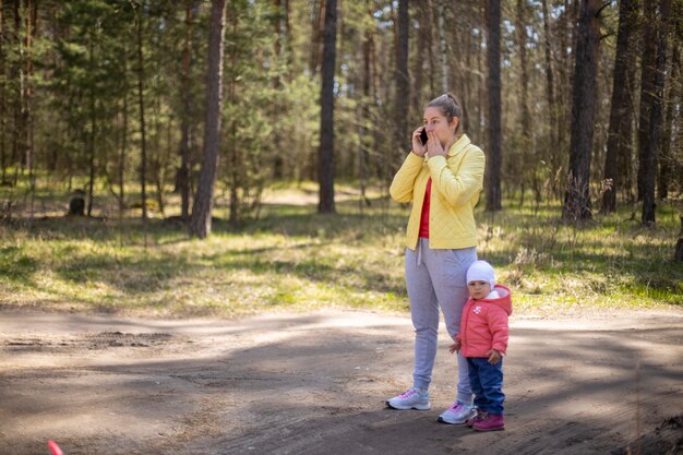 young woman with a baby toddler talking on a mobile phone emotionally in a forest outside the city 4g