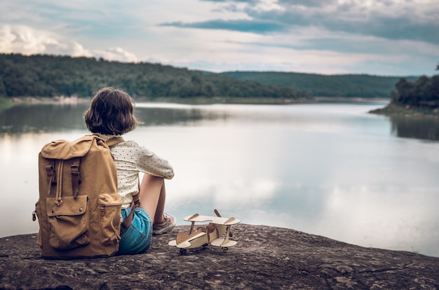 Young woman with backpack and airplane model by the lake