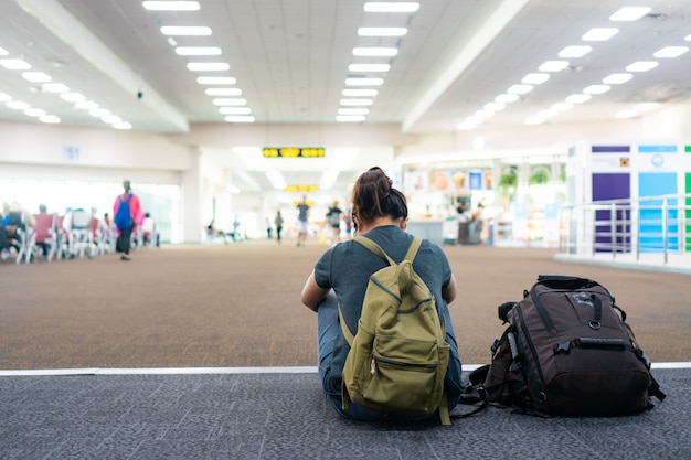 飛行機の時刻表の近くの空港にバックパック付きの若い女性