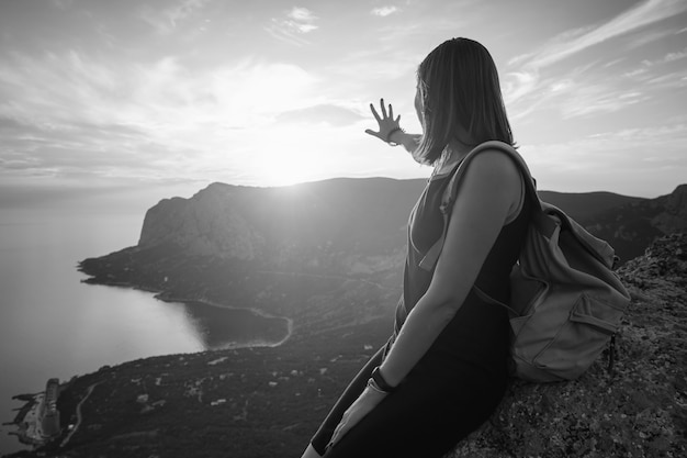 バックパックを持った若い女性は、日没時に山と海の景色を楽しんでいます。ライフスタイルの感情的な概念の休暇週末の逃走空中クリミアの風景