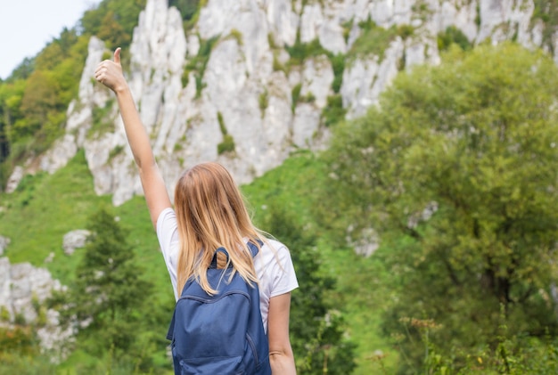 Young woman with backpack giving thumbs up. Trekking and tourism concept.