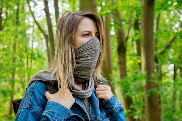 Young woman with backpack hide face with a scarf in a mixed forest Beskidy in Poland in spring time.