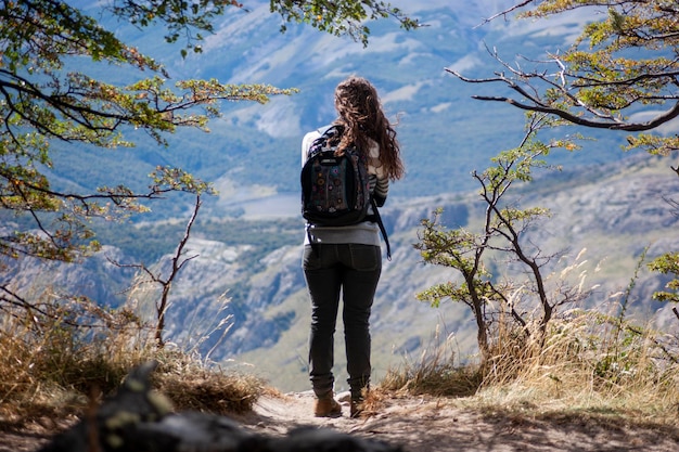 写真 山岳風景を観察するハイキング中に休憩するバックパックを背負った若い女性