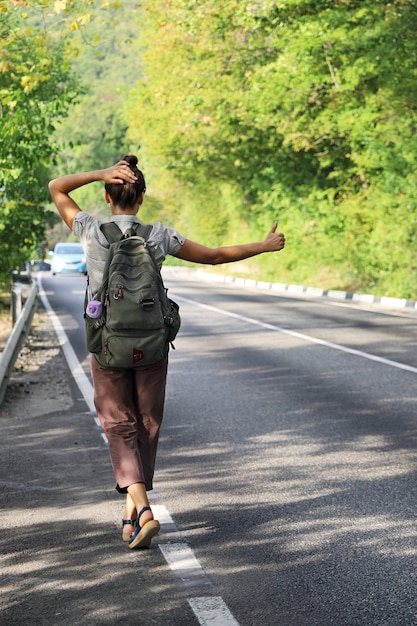 Young woman with backpack tries to stop passing car to hitchhike