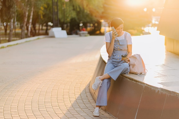 Young woman with backpack using  smartphone with  at sunset.