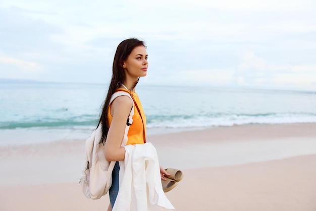 Молодая женщина с рюкзаком гуляет по пляжу на летних каникулах на острове у океана на Бали